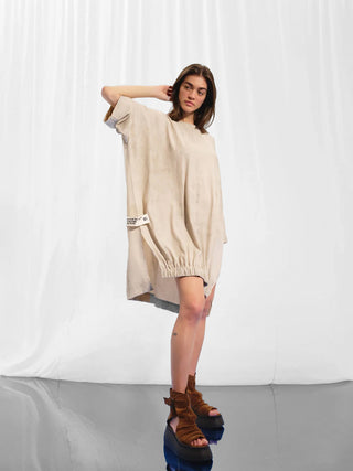 Frau trägt #VDR Tunica beige, oversized mit weiten halblangen Ärmeln und elastischem Saum. Sie posiert in braunen Sandalen, betont die lässige, urbane Silhouette der Tunika.