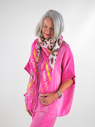 Eine Frau trägt das OFF#DLY Tuch 130x130 leo pink aus 100% Viskose, gestylt als modisches Accessoire um den Hals. Das Tuch zeigt ein dezentes Leopardenmuster.