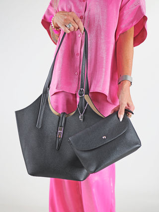 Diana & Co Firenze Bag black: Frau hält zwei Taschen, darunter eine schwarze Diana & Co Tasche aus Kunstleder mit silberner Schnalle und praktischem Riemenverschluss, der leicht zu öffnen ist.