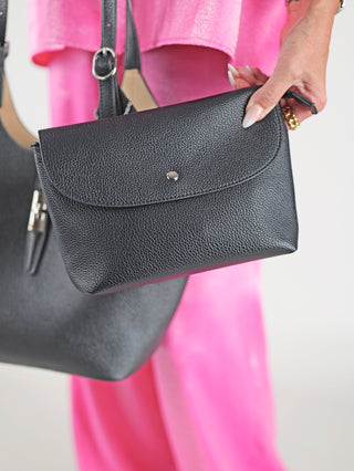 Frau hält die Diana & Co Firenze Bag schwarz, eine elegante Kunstleder-Handtasche mit Magnetverschluss, ideal für Alltag und besondere Anlässe. Enthält eine herausnehmbare Innentasche für zusätzlichen Stauraum.