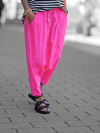 Person trägt OFF#DLY Harem Pant Leyla pink, mit lockerer Passform und großen Taschen, kombiniert mit Sandalen. Die Hose besteht aus Baumwoll-Leinen-Mix und bietet urbanen, lässigen Stil.