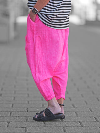 Person trägt OFF#DLY Harem Pant Leyla pink, locker geschnittene Hose mit tiefem Sitz, sichtbaren aufgesetzten Taschen und flexiblem Bund, kombiniert mit gestreiftem Shirt, betont lässigen, urbanen Stil.