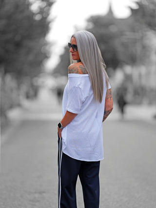 Weißes OFF#DLY Shirt Luisa mit Oversize-Schnitt, überschnittener Schulter und asymmetrischem Saum. Weicher Baumwoll-Elasthan-Mix, vielseitig kombinierbar, lässig über eine Schulter tragbar. Ideal für entspannte Looks.
