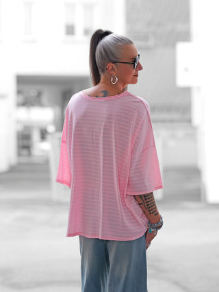 Nahaufnahme des OFF#DLY Stripes Shirt rosa/pink, getragen von einer Frau. Das Streifenmuster und der Herz-Print l’amore è bello am Saum sind sichtbar und verleihen dem Shirt einen stilvollen Look.