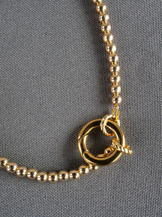 Kugelkette vario 100 cm schmal goldfarben, bestehend aus kleinen, glänzenden goldfarbenen Perlen mit einem runden Verschluss und gedrehtem Ring, präsentiert auf grauem Stoff. Allergie- und nickelfrei, kürzbar.