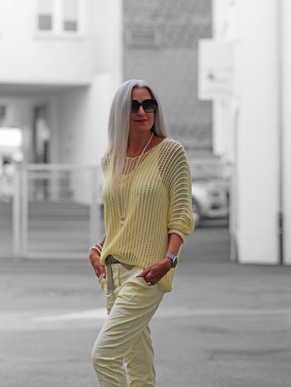 Nahaufnahme einer Hand in einer Tasche, einer Person mit Sonnenbrille und einer Person mit Uhr, die den OFF#DLY Netzpulli Treviso butteryellow tragen, mit luftiger Netzoptik und angenehmem Materialmix.