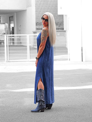 Eine Frau trägt das OFF#DLY Kleid Caorle blau mit Spaghettiträgern, das locker fällt und aus Baumwolle besteht, ideal für entspannte Sommertage.