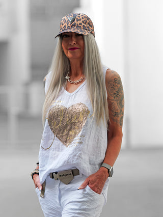 Frau trägt OFF#DLY Top Belive white mit glitzerndem Paillettenherz und inspirierendem Print, kombiniert mit einem modischen Hut und einer Uhr, betont lässigen und modernen Stil.