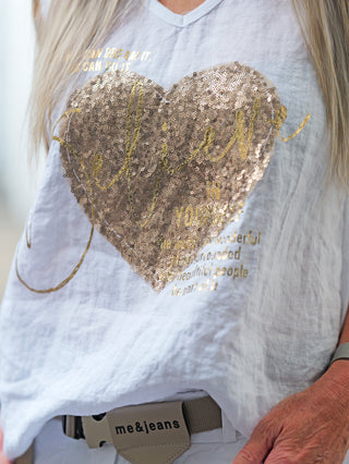 Nahaufnahme des OFF#DLY Top Belive white: Ein weißes Shirt mit glitzerndem Paillettenherz und inspirierendem Print believe in yourself, getragen von einer Person, ideal für einen lässigen, modernen Look.