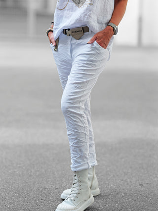 Nahaufnahme eines weißen Schuhs neben der OFF#DLY Pant Lennox white, einer lässigen Jogpant in Beige mit Gürtel und Crinkle-Look, perfekt für entspannte, stilvolle Freizeitlooks.