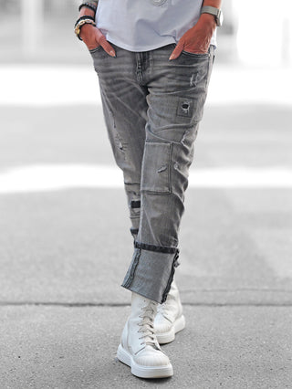 Nahaufnahme der OFF#DLY Black Denim Cesenatico, getragen von einer Person in einem weißen Hemd, zeigt auffällige Nähte und Destroy-Elemente, kombiniert mit ausgefransten Umschlägen für einen modischen Look.
