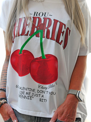 Frau trägt das OFF#DLY Tee Cherry white mit roten Kirsch-Print. Lockerer Schnitt, Rundhalsausschnitt; perfekt für lässige Sommeroutfits. Ideal zu Jeans oder Shorts kombinierbar.