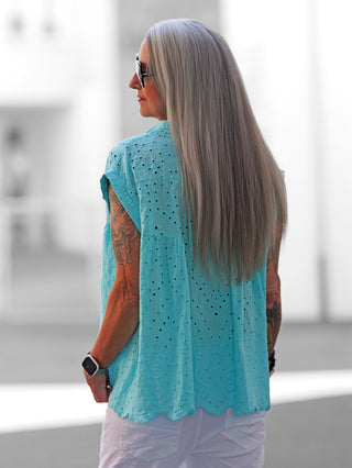 Nahaufnahme der OFF#DLY Bluse Orea türkis mit feiner Lochstickerei und geschwungener Saumkante, die einen femininen, mediterranen Look erzeugt; ideal für luftige Sommeroutfits.