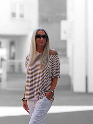 Eine Frau trägt das OFF#DLY Margot Stripe Tee in Weiß/Taupe mit Rundhalsausschnitt und geschnittenen Kanten, kombiniert mit Sonnenbrille, ideal für Street-Fashion-Looks.