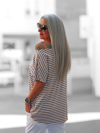 Nahaufnahme des OFF#DLY Margot Stripe Tee in Weiß/Taupe mit Rundhalsausschnitt und geschnittenen Kanten, getragen von einer Person im Freien, sichtbar sind auch ein Tattoo und Sonnenbrillen.
