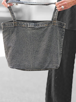 Person hält OFF#DLY Bag Sunset Ibiza aus verwaschenem schwarzem Denim mit robusten Henkeln, Größe 40x30x15 cm. Die Tasche wirkt leer oder leicht gefüllt.