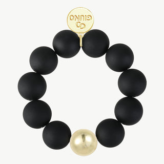 Das OFF#DLY Acrylarmband Kugel black zeigt zehn matte schwarze Perlen und eine glänzende goldene Kugel, ergänzt durch einen kleinen goldenen Charm mit GINNO-Gravur.