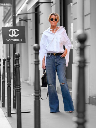 Eine Frau trägt die Gitta Banko Bluse Jacqueline, kombiniert mit blauer Jeans und Sonnenbrille, die durch klassischen Kragen und Knopfleiste zeitlose Eleganz und Vielseitigkeit ausstrahlt.