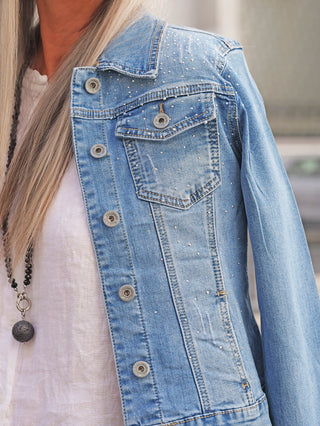 Torso in der OFF#DLY Jacke Palermo midblue, verziert mit feinen Strassdetails, getragen über einer weißen Bluse, akzentuiert von einer langen Halskette mit dunklem Steinanhänger.