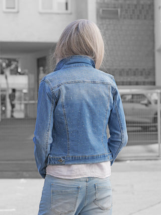 Person trägt die OFF#DLY Jacke Palermo midblue, eine hellblaue Strass-Denimjacke mit klassischer Silhouette, verziert mit Strasssteinen, geschlossen mit Knopfleiste, kombiniert mit Jeans und weißem Shirt.
