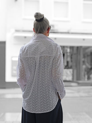 Frau trägt True Religion Drop Shoulder Blouse mit Lochstickmuster und lässigem Schnitt. Diese Bluse aus 100% Baumwolle bietet einen entspannten Look und vielseitige Styling-Möglichkeiten.