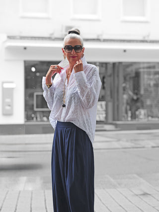 Nahaufnahme einer Frau mit Sonnenbrille, die die True Religion Drop Shoulder Bluse trägt. Die Bluse zeigt ein edles Lochstickmuster und einen lässigen Schnitt mit leicht verlängertem Rückenteil.