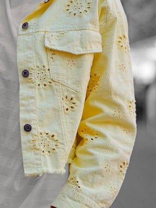 Nahaufnahme der OFF#DLY Jacke Lipari gelb mit Lochstickerei, dunklen Knöpfen, über weißem T-Shirt getragen. Die floralen Details und der leicht oversize Schnitt betonen den sommerlichen Denim-Stil.