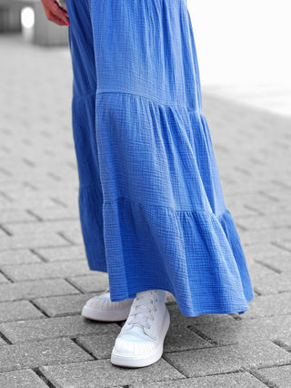 Nahaufnahme des OFF#DLY Kleid Bergamo blau mit smock-elastischem Oberteil und stufigem Rock, getragen zu Sneakern auf einem Boden. Ideal für sommerliche Anlässe.