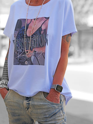 Person trägt das OFF#DLY Tee Destination white mit Leoparden-Print und DESTINATION runway Schriftzug, kombiniert mit locker sitzenden Jeans, Perlenkette und Smartwatch, im lässigen Streetstyle-Look.