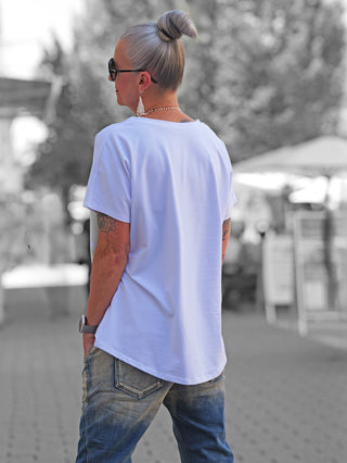 Frau von hinten, trägt OFF#DLY Tee Destination white; weißes T-Shirt mit DESTINATION Runway-Print, lockerer Schnitt, kombiniert mit Jeans, Schmuck und Accessoires, vermittelt einen lässigen, modischen Straßenlook.
