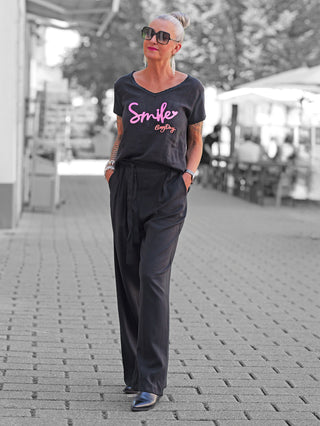 Nahaufnahme der OFF#DLY Pant Cagliari black, getragen von einer Frau mit schwarzem Shirt. Die Hose zeigt eleganten, weiten Schnitt mit Bundfalten und elastischem Gummizug für sommerlichen Komfort.