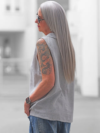 Person mit langen silbergrauen Haaren trägt das ärmellose OFF#DLY Blusenshirt Lavena lightgrey, kombiniert mit blauer Jeans. Sichtbare Details: weicher Kragen, lockerer Schnitt, ideal für warme Tage.
