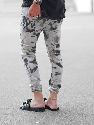 Nahaufnahme eines Fußes, der die OFF#DLY Denim Castiglione in grau/schwarz trägt. Die Jeans zeigt einen modernen Batik-Stil mit schmal zulaufender Passform und leicht gerafftem Beinabschluss.
