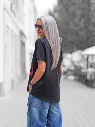 Eine silberhaarige Frau trägt das OFF#DLY Shirt Pozzallo darkblue, ein locker sitzendes, elegantes Viskose-T-Shirt mit V-Ausschnitt und leicht überschnittenen Schultern, auf einer urbanen Straße.