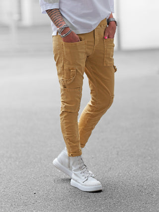 OFF#DLY Joggpant Marliana camel mit schmalem Schnitt und Cargotaschen, verziert mit Nieten. Getragen mit hochgekrempelten Beinen und kombiniert mit weißen High-Top-Sneakern für einen urbanen Look.