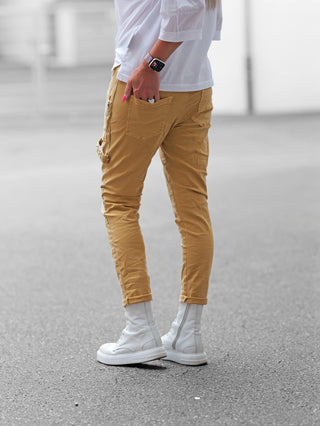 Eine Person trägt die OFF#DLY Joggpant Marliana camel, schmal geschnitten und bis zum Knöchel gekrempelt, kombiniert mit weißen High-Top-Boots und einem weißen T-Shirt.