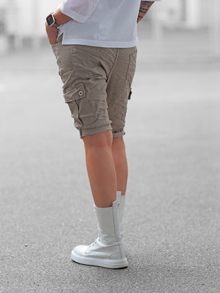 Person trägt OFF#DLY Short Lecce khaki, knielange Cargoshorts mit Seitenklapptaschen, kombiniert mit weißen, mittelhohen Schnürstiefeln. Sichtbar sind auch ein Smartwatch am Handgelenk und ein tätowierter Unterarm.