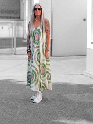 Frau in OFF#DLY Kleid Milano khaki/multi mit farbigen Kreismustern, trägt weiße High-Top-Sneakers und Accessoires, steht auf Straße vor hellem Gebäude.