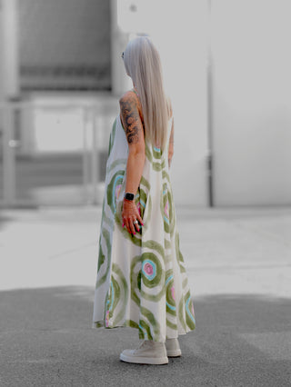 Person mit langem, silber-grauem Haar trägt ein OFF#DLY Kleid Milano khaki/multi, ein luftiges, bodenlanges Sommerkleid mit buntem Kreismuster, kombiniert mit weißen High-Top-Sneakern.