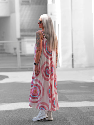 Ältere Frau trägt das OFF#DLY Kleid Milano rosa/multi, ein luftiges, knöchellanges Sommerkleid mit großen, bunten Kreismotiven, kombiniert mit weißen Sneakers und einem Smartwatch.