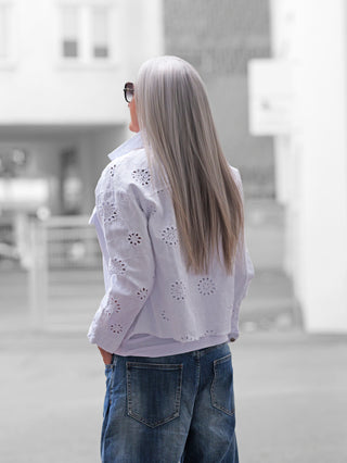 Person von hinten mit langen, silbrig-grauen Haaren und Sonnenbrille. Sie trägt die OFF#DLY Jacke Lipari white, eine weiße Bluse mit Lochstickerei, kombiniert mit entspannten blauen Jeans.