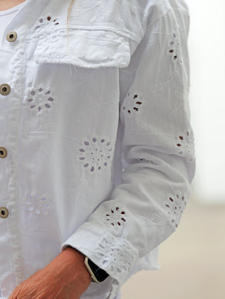 Nahaufnahme einer Person, die die OFF#DLY Jacke Lipari white trägt, aus leichtem, augenstickereiverspieltem Stoff. Die Jacke hat einen Button-Front und bietet einen lässigen, modernen Oversize-Look.