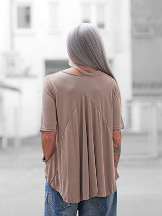 Person mit langen, silbernen Haaren trägt das OFF#DLY T-Shirt Agropoli beige, das durch fließende Falten im Rücken und Taschen an der Seite besticht. Lockerer Schnitt über Denim.