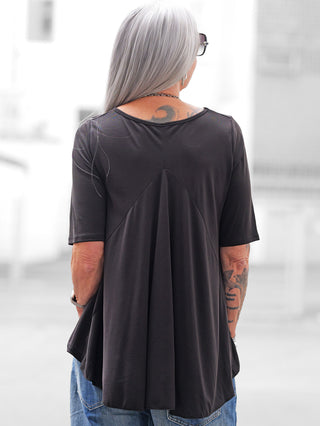 Person von hinten mit schulterlangem grauem Haar trägt das OFF#DLY T-Shirt Agropoli black mit dreieckigem Rückenteil, kombiniert mit blauer Jeans. Sichtbare Tattoos und silberne Accessoires ergänzen den Look.