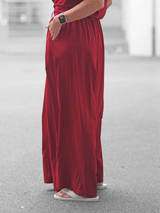 Die OFF#DLY Pant Gallipoli red zeigt einen eleganten Palazzo-Stil mit luftiger Weite, elastischem Bund und praktischen Taschen, getragen mit weißen Flip-Flops auf einem Gehweg.