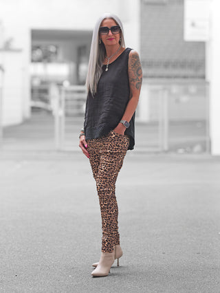 Frau trägt OFF#DLY Joggpant Brindisi Leo braun/black, kombiniert mit schwarzem Top und beigen Stiefeletten. Die Hose im Leo-Look sitzt locker und ist durch elastischen Bund komfortabel.