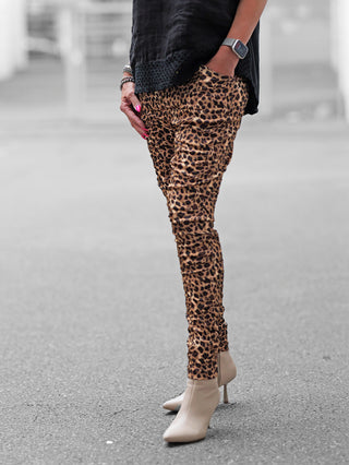 Person trägt die OFF#DLY Joggpant Brindisi Leo braun/black in Leopardenmuster, kombiniert mit beigen, spitzen Ankle Boots. Sichtbar sind auch eine schwarze Oberteilkante und Accessoires am Handgelenk.