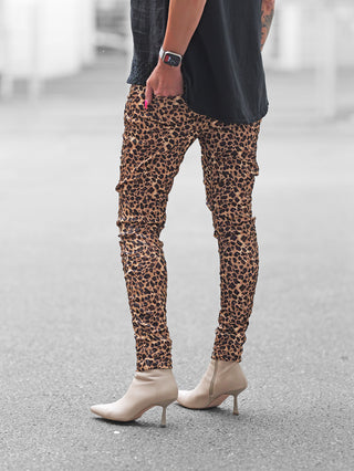 Person in OFF#DLY Joggpant Brindisi Leo braun/black, enge Leoparden-Leggings, kombiniert mit creme-beigen, spitz zulaufenden Stiefeletten, leicht erkennbares schwarzes Oberteil, Uhr und kleines Unterarm-Tattoo sichtbar.