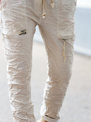 Nahaufnahme der OFF#DLY Pant Iseo beige, eine schmal geschnittene, leichte Joggpant mit Kordelzug, seitlichen Cargotaschen und Crinkle-Optik, ideal für einen urbanen, sportlichen Look.
