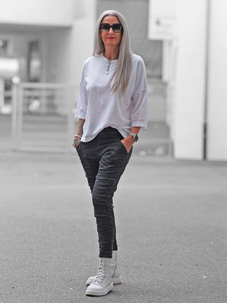 Frau in urbanem Umfeld trägt OFF#DLY Joggpant Vellano black denim, kombiniert mit weißem Oversized-T-Shirt und klobigen weißen Stiefeln, zeigt den schmalen Schnitt und urbanen Look der Hose.